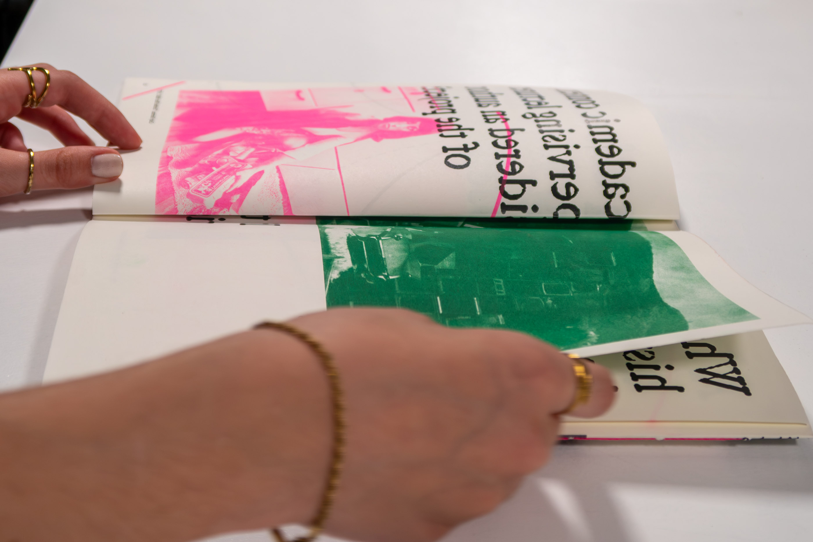 Hands folding a page printed with pink and green risograph ink over a portrait photograph.